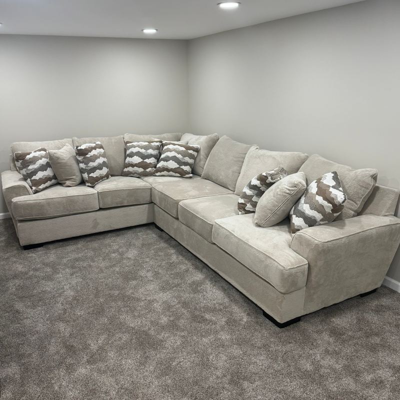 Finished basement room with gray carpet, recessed lights and a sectional sofa