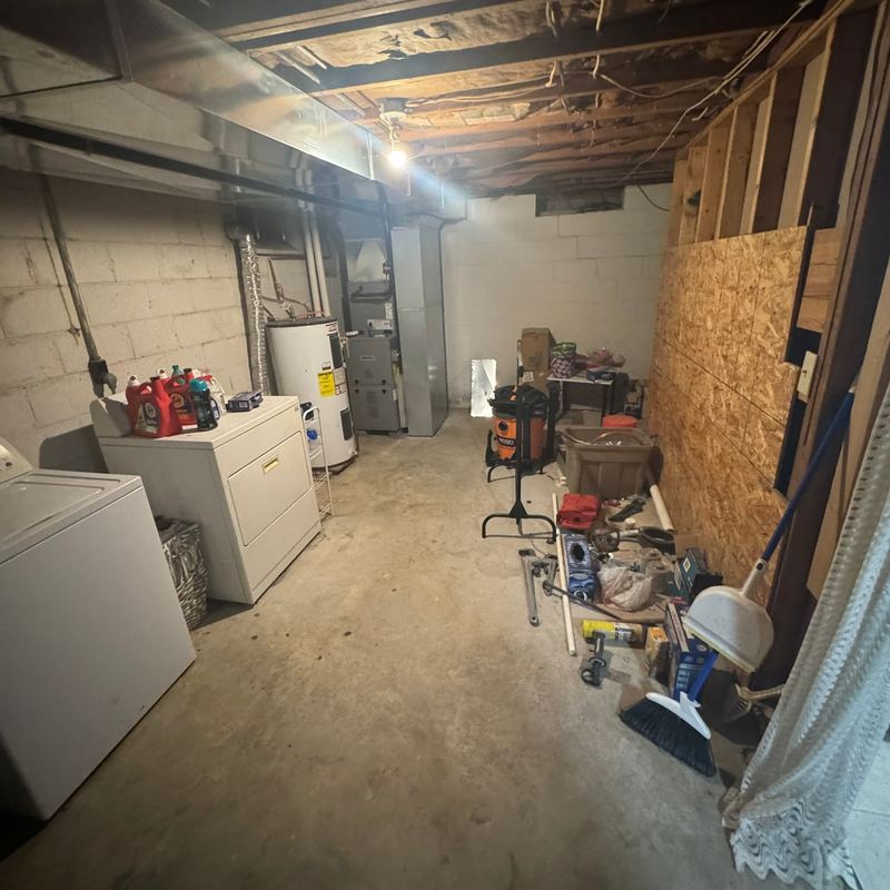 Unfinished basement with a washer, dryer and stored tools on a bare concrete floor