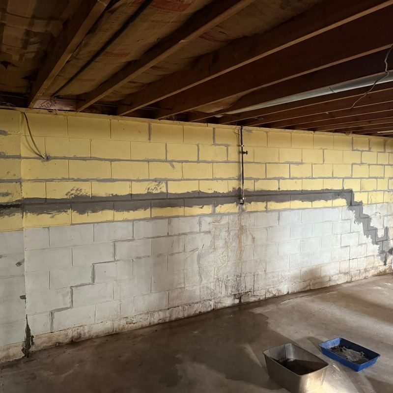 Bare block basement walls with a long stair step crack and water stains