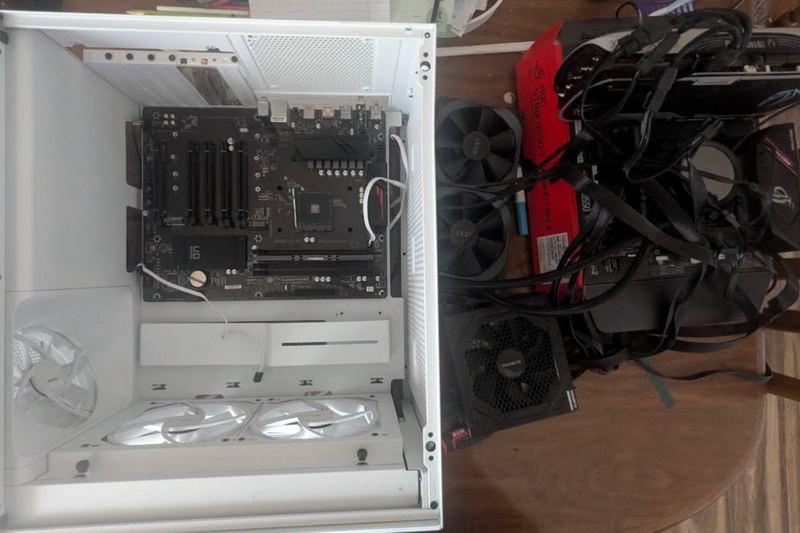 A white computer case opened up on a table, the motherboard in it and the other parts set out beside it
