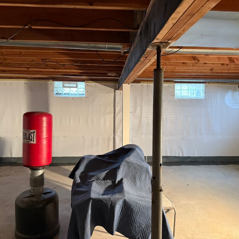 Basement walls covered in white waterproofing, with a support post and a punching bag